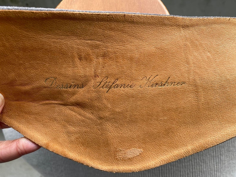 May include: Close-up of a brown leather patch with the text "Versace Stefanie Kostenko" written in black ink.