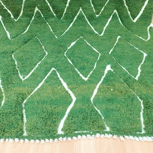 May include: A green and white rug with a geometric pattern. The rug has a fringe border.