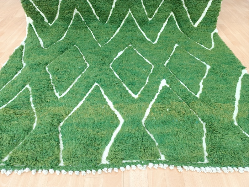 May include: A green and white rug with a geometric pattern. The rug has a fringe border.