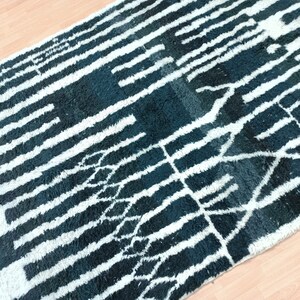 May include: A black and white rug with a geometric pattern. The rug has a long, narrow shape and is made of a soft, fluffy material.