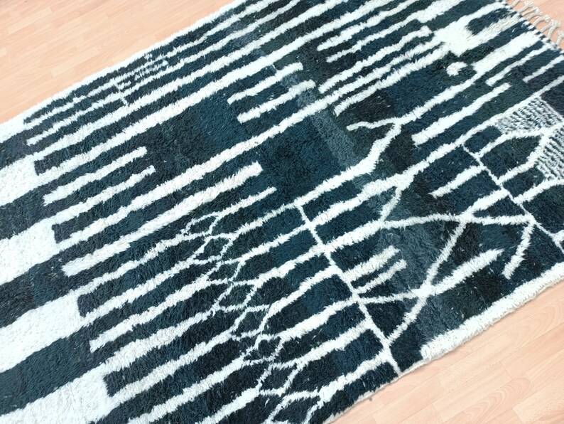 May include: A black and white rug with a geometric pattern. The rug has a long, narrow shape and is made of a soft, fluffy material.