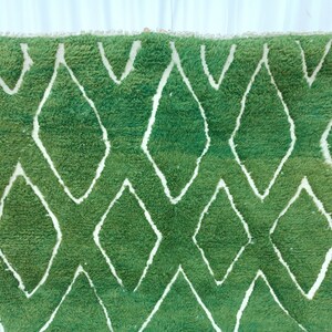 May include: Green and white Moroccan rug with a diamond pattern. The rug is made of wool and has a soft, fluffy texture.