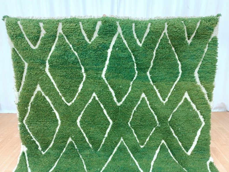 May include: Green and white Moroccan rug with a diamond pattern. The rug is made of wool and has a soft, fluffy texture.
