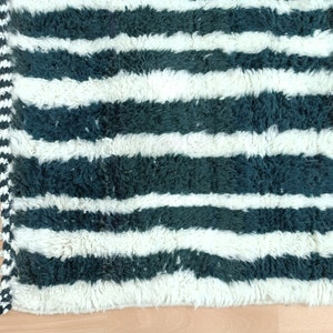 May include: A white and dark green striped rug with fringe on one side. The rug is made of a soft, fluffy material.