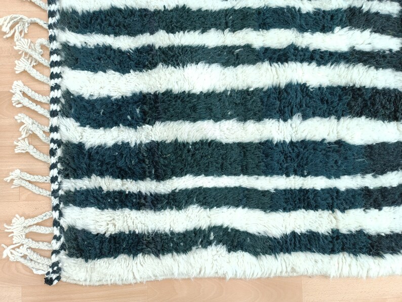 May include: A white and dark green striped rug with fringe on one side. The rug is made of a soft, fluffy material.