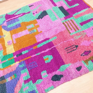 K&ouml;nnte beinhalten: Ein bunter, abstrakter Teppich mit geometrischen Formen in den Farben Rosa, Gr&uuml;n, Lila, Orange und Schwarz. Der Teppich ist aus einem weichen, flauschigen Material gefertigt.