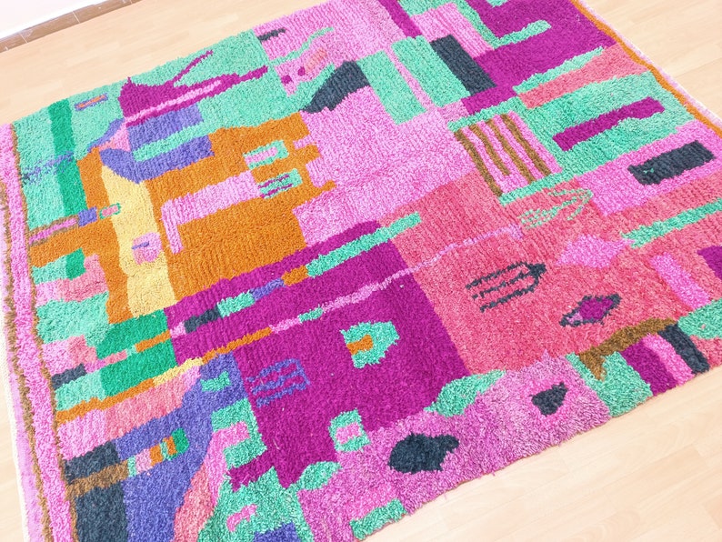K&ouml;nnte beinhalten: Ein bunter, abstrakter Teppich mit geometrischen Formen in den Farben Rosa, Gr&uuml;n, Lila, Orange und Schwarz. Der Teppich ist aus einem weichen, flauschigen Material gefertigt.