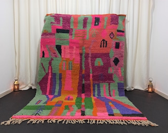 May include: A colourful Moroccan rug with geometric patterns in shades of pink, green, purple, orange, and black. The rug has a fringed border.