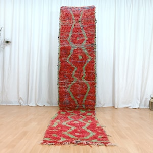 May include: A long, red and green Moroccan rug with a geometric pattern. The rug is fringed on both ends and has a distressed look.
