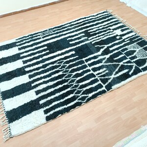 May include: Black and white Moroccan rug with a geometric pattern. The rug has a fringe border and is made of wool.