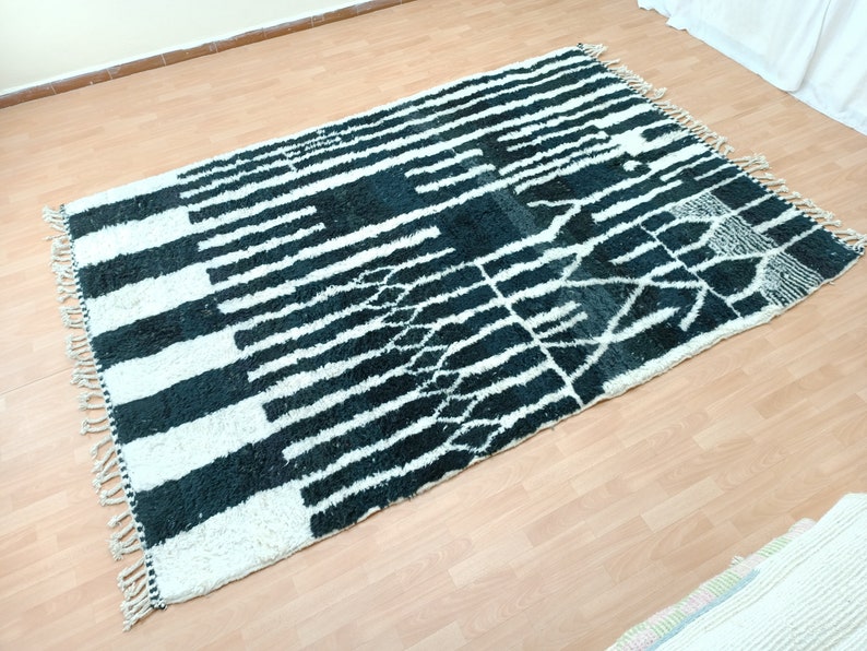 May include: Black and white Moroccan rug with a geometric pattern. The rug has a fringe border and is made of wool.