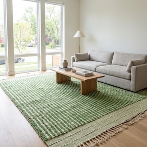May include: A large rectangular area rug featuring a pattern of horizontal green and cream stripes with a textured, tufted surface. The rug includes a wide border with a braided design and long, knotted fringe along the bottom edge.