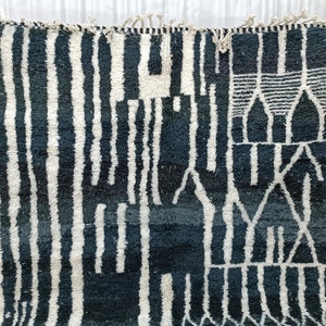 May include: A black and white Moroccan rug with a geometric pattern. The rug has a fringe border and is made of wool.