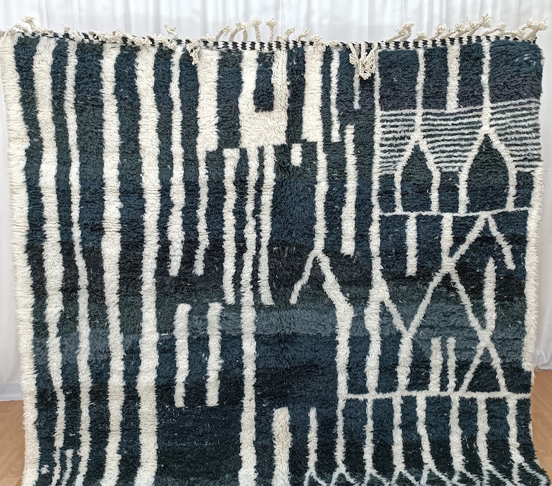 May include: A black and white Moroccan rug with a geometric pattern. The rug has a fringe border and is made of wool.