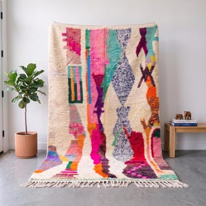 May include: A large rectangular area rug with a cream-coloured base featuring a vibrant, multi-coloured abstract pattern of vertical stripes, geometric diamond shapes, and jagged lines in shades of hot pink, orange, teal, purple, and green with fringe.