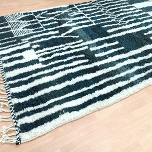 May include: A black and white striped rug with a geometric pattern. The rug has a fringe border and is made of a soft, fluffy material.