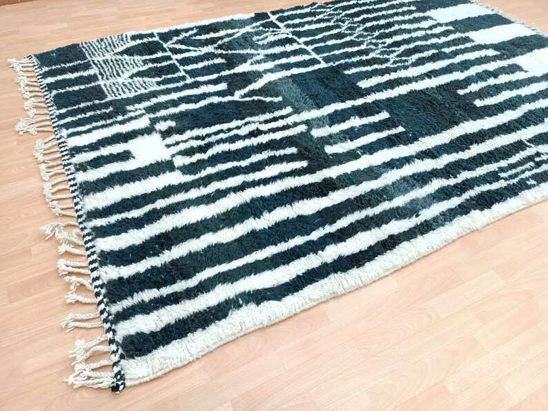 May include: A black and white striped rug with a geometric pattern. The rug has a fringe border and is made of a soft, fluffy material.