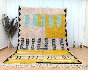May include: A hand-woven rug with a geometric pattern in shades of pink, yellow, blue, black, and white. The rug has a fringe border.