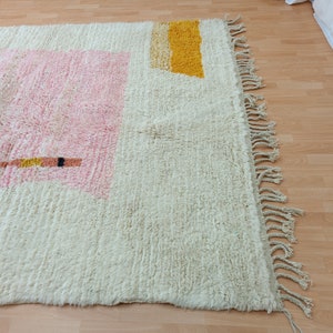May include: A white, cream, pink, and yellow geometric patterned rug with fringe on the edges.