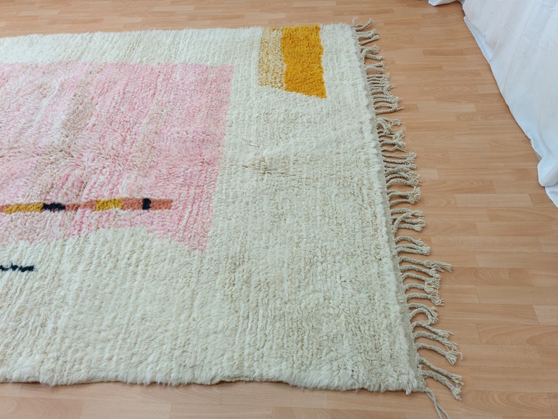 May include: A white, cream, pink, and yellow geometric patterned rug with fringe on the edges.