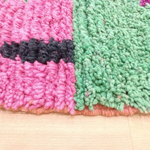 K&ouml;nnte beinhalten: Nahaufnahme eines rosa, gr&uuml;nen und schwarzen Teppichs mit einer flauschigen Textur. Der Teppich hat einen gewebten Rand.