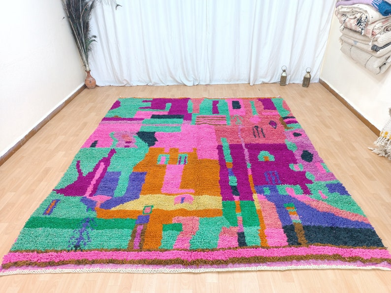 K&ouml;nnte beinhalten: Ein bunter, abstrakter Teppich mit geometrischen Formen in den Farben Rosa, Gr&uuml;n, Orange, Lila und Blau. Der Teppich hat einen Fransenrand.