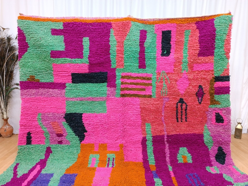 K&ouml;nnte beinhalten: Ein farbenfroher, abstrakter Teppich mit geometrischen Formen in den Farben Pink, Gr&uuml;n, Orange, Lila und Schwarz. Der Teppich ist aus einem dicken, strukturierten Material gefertigt und hat ein handgewebtes Aussehen.