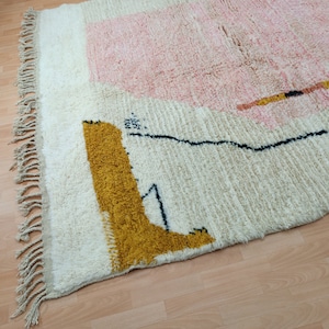 May include: A white rug with a pink, yellow, and black geometric design. The rug has a fringe border.
