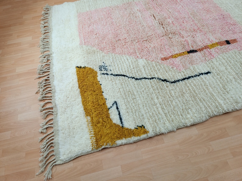 May include: A white rug with a pink, yellow, and black geometric design. The rug has a fringe border.