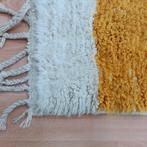 May include: A white and yellow woven rug with fringe on the edges. The rug has a simple design with two colors.