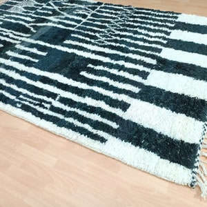 May include: A white and dark green Moroccan rug with a geometric pattern. The rug has a fringe border.