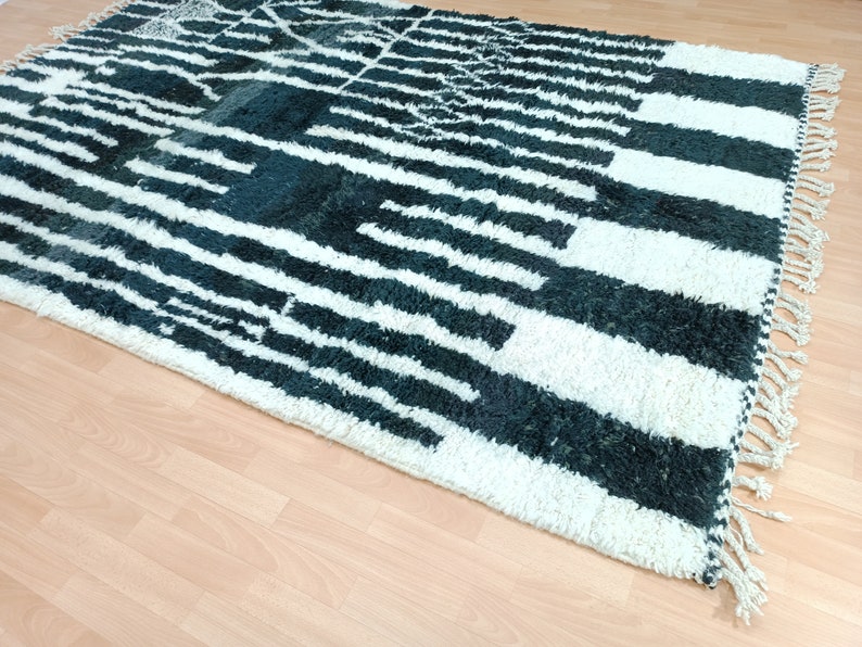 May include: A white and dark green Moroccan rug with a geometric pattern. The rug has a fringe border.