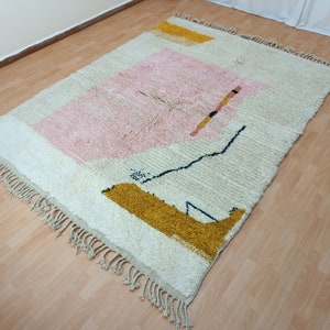 May include: A white, cream, pink, and yellow geometric patterned rug with a fringe border.