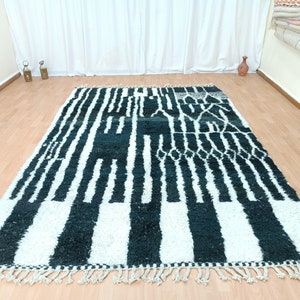 May include: Black and white striped rug with a geometric pattern. The rug has a fringed border.