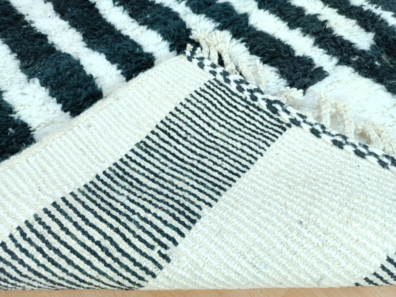 May include: Close-up of the back of a black and white striped rug with a black and white woven border. The rug is made of a soft, fluffy material.