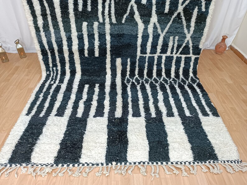 May include: A black and white Moroccan rug with a geometric pattern. The rug has a fringe border and is made of wool.
