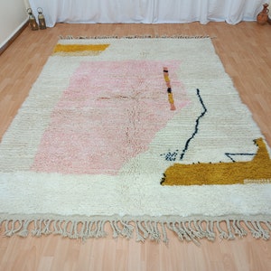 May include: A white, pink, and yellow geometric patterned rug with fringe. The rug has a modern abstract design.
