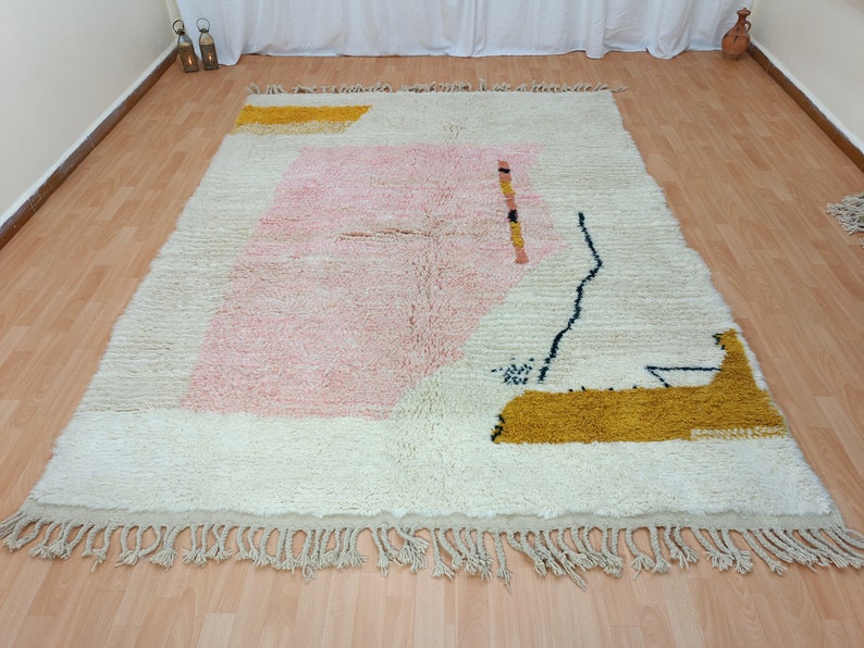 May include: A white, pink, and yellow geometric patterned rug with fringe. The rug has a modern abstract design.