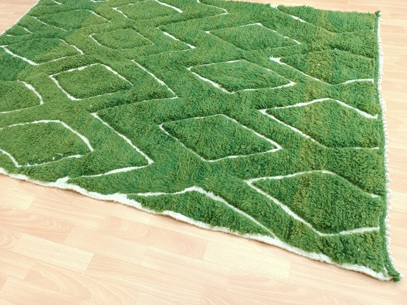 May include: A green and white geometric patterned rug with a white border. The rug is made of a soft, plush material.
