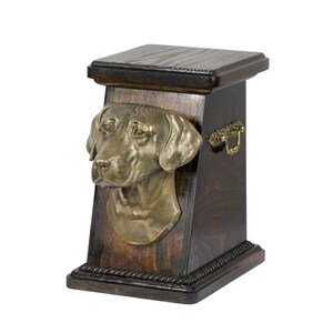 May include: A wooden pet urn with a bronze dog head sculpture on the front. The urn has a dark wood finish and a brass handle.