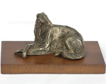 May include: A bronze sculpture of a dog lying down on a wooden base. The dog is facing to the right and has its head tilted up. The sculpture is a realistic depiction of a dog.