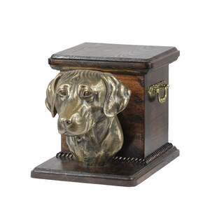 May include: A wooden pet urn with a bronze Labrador Retriever head sculpture on the front. The urn has a dark wood finish and a brass handle.