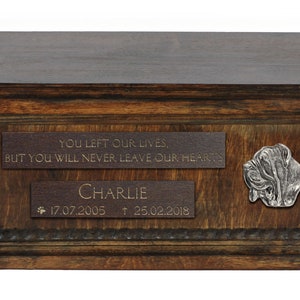 Op de afbeelding: Een houten dierenurne met een tinnen hondenkop ornament. De urne heeft twee gegraveerde plaquettes met de tekst "You left our lives, but you will never leave our hearts" en "Charlie 17.07.2005 † 25.02.2018".