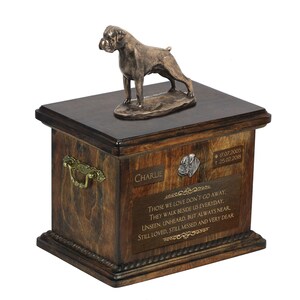 May include: A wooden pet urn with a bronze Boxer dog figurine on top. The urn has a brass handle and a plaque with the name "Charlie" and dates "17.07.2005 † 25.02.2018". The plaque also includes a quote: "Those we love don't go away, they walk beside us everyday, unseen, unheard, but always near, still loved, still missed and very dear."