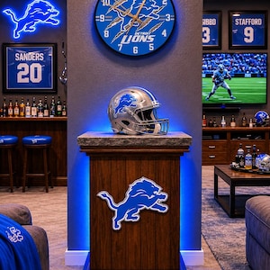 May include: A silver Detroit Lions football helmet sits on a wooden pedestal with a blue LED light. Above it, a round wall clock features the team logo with claw marks. The pedestal displays a large blue and white Detroit Lions lion emblem.