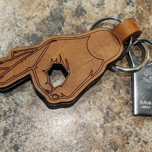 May include: A brown leather keychain shaped like a hand making the "OK" gesture. A silver USB drive with the text "64GB USB 3.0" is attached to the keychain.