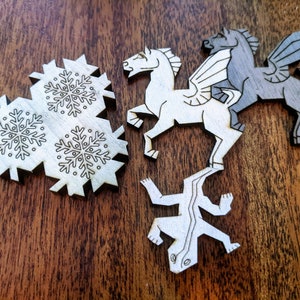May include: Three wooden cutouts of a white horse, a gray winged horse, and a white lizard. The horse cutouts are in a standing position, while the lizard cutout is lying on its belly. The cutouts are on a brown wooden surface.