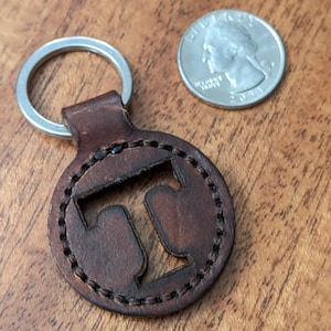 May include: Brown leather keychain with a cut-out letter T. The keychain is attached to a silver key ring.