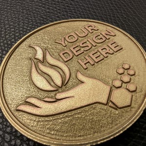 May include: A gold-colored metal round plaque with a raised design of a hand holding a flame. The text "YOUR DESIGN HERE" is embossed on the plaque.
