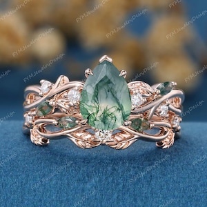 May include: A rose gold ring set featuring a pear-shaped green moss agate center stone. The ring is accented with small white diamonds and green gemstones, with a delicate leaf and vine design.
